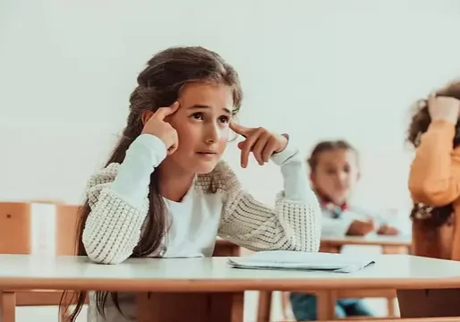 The girl sitting confusedly with her hands on her head in the school desk and attends clas